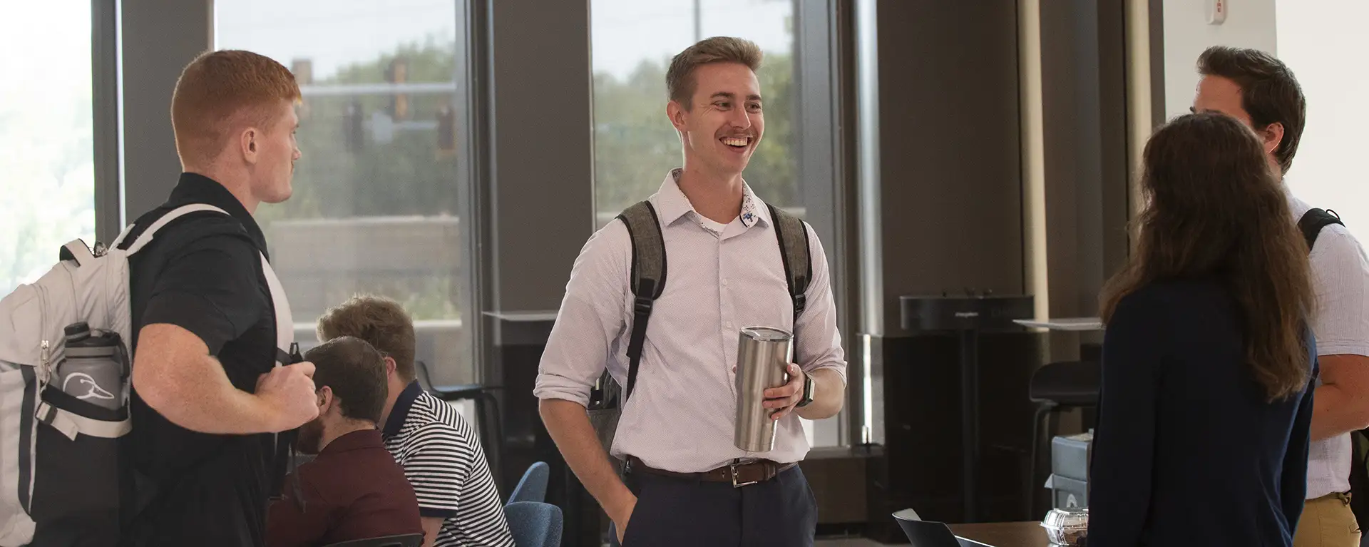 A student dressed professionally smiles and talks with his peers in the lobby.