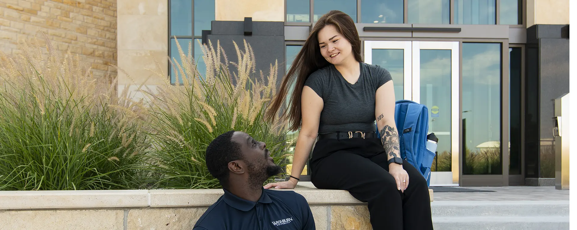 Two students sit on steps outside Dole Hall chatting. 