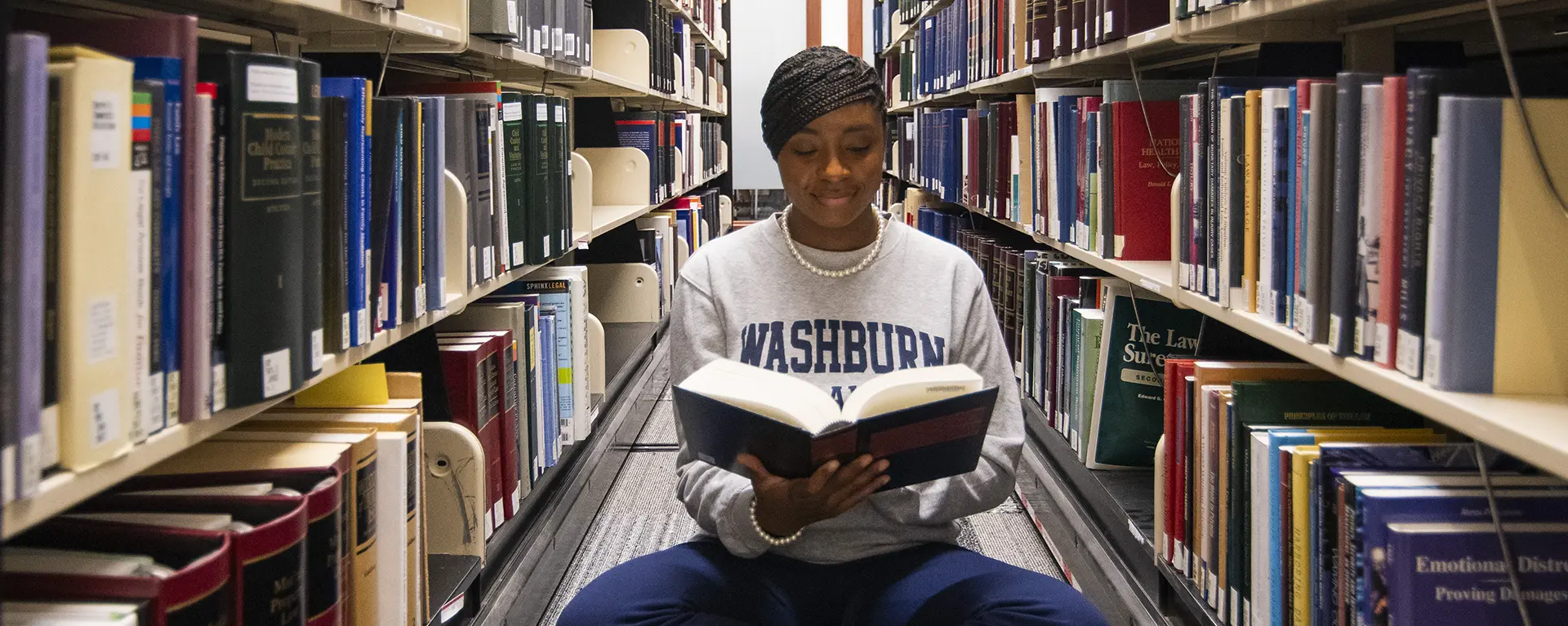 A student reads a book in the stacks at the library. 