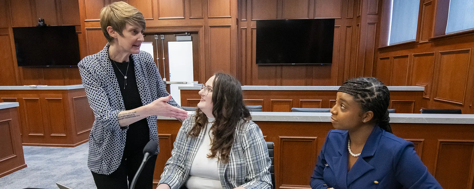 A law professor explains a comment to two law students while in the trial courtroom.