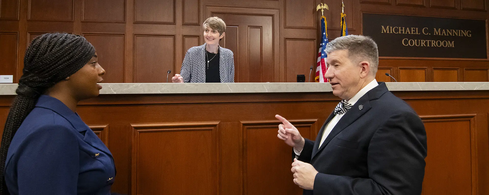 Faculty members coach a student preparing for a competition in the courtroom. 