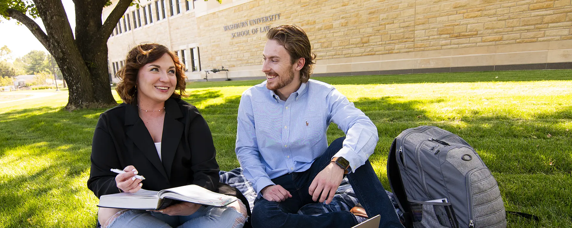 Two students study under a tree outside on a nice day.