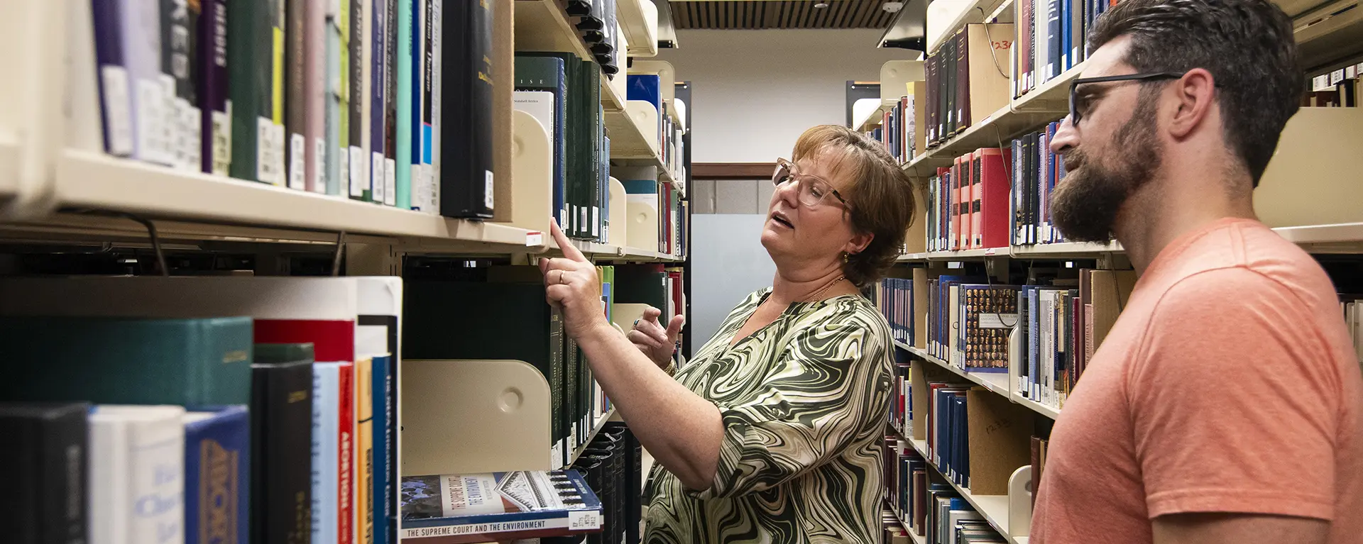 A librarian helps a student find a book on the shelf.