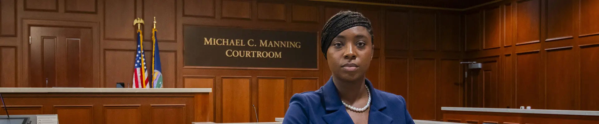 Student stands in front of courtroom prepared for competition. 