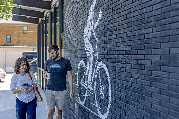 A couple smiles and walks with cups of coffee in front of a mural of a business logo for Circle Coffee.