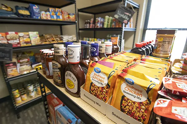 Barbecue sauce and seasonings sit on a shelf with shelves of food behind.