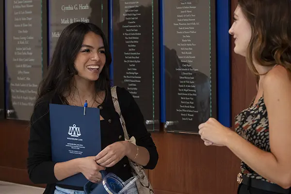 Two students holding law materials talk outside of classroom. 