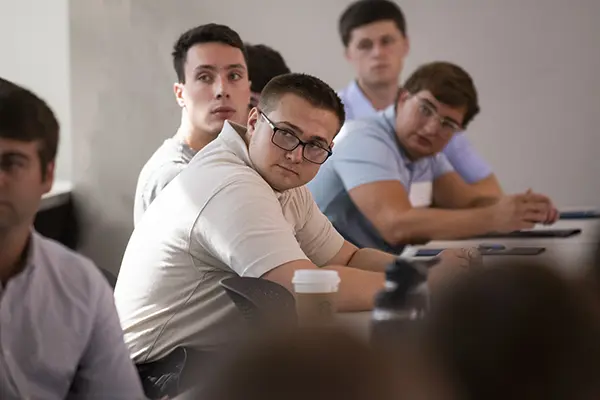 A group of students in class look toward a speaker. 