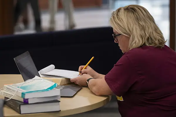 A student takes notes while studying at a table in the library.