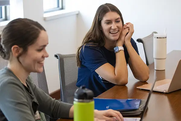 Two students sit at a table in a study room. 