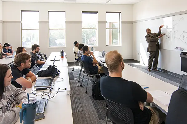 Law professor at whiteboard teaching students concepts during class. 