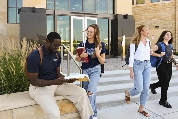 Two students chat outside Dole Hall while two students walking down steps talk.