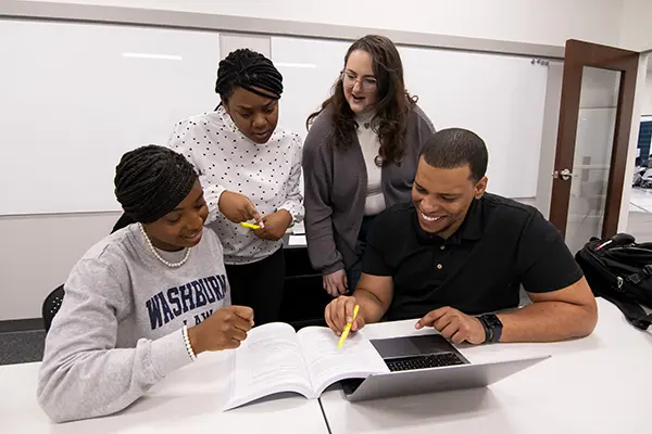 Students gather around course material while studying and laughing. 