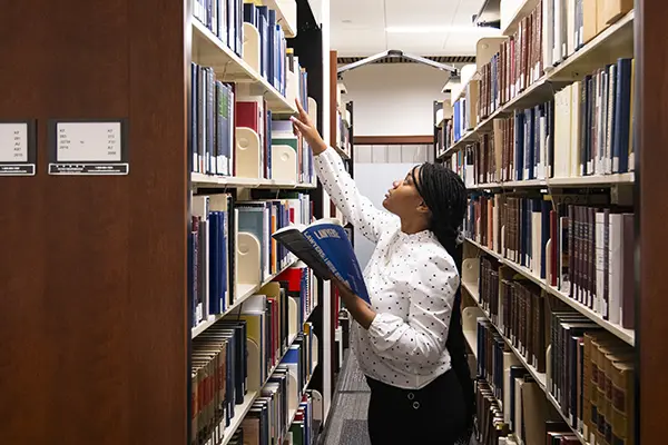 A student reaches for a book on a law library bookshelf.