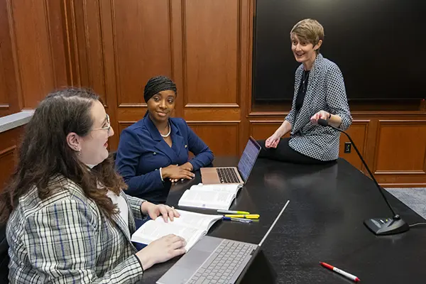 A law professor works with two students in the trial courtroom.