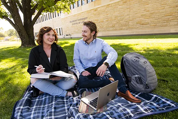 Students chat and smile while studying outside on a nice day.