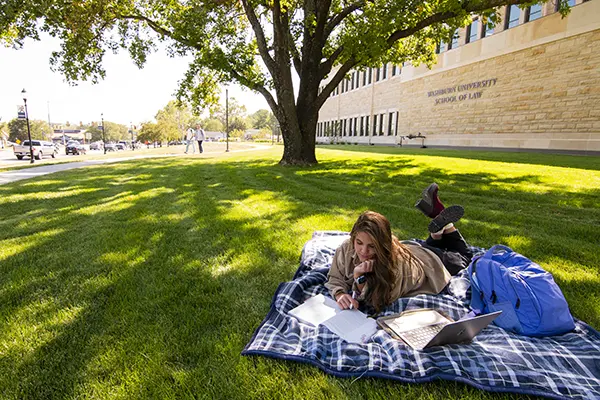 student writing outdoors on blanket with books and paper