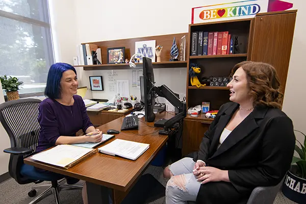 A dean visits with a student across a desk in her office.