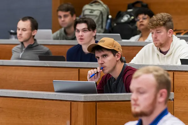 A law student chews on his pen while taking notes in class.