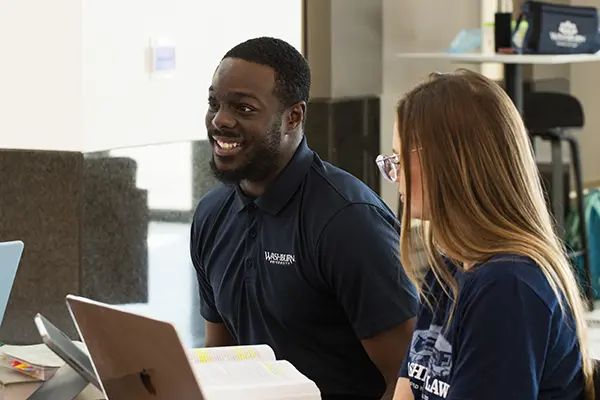 A student smiles while talking with other students at a table in the lobby.