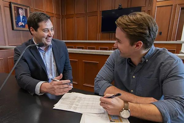 A law student smiles while working with a professor in a courtroom classroom.