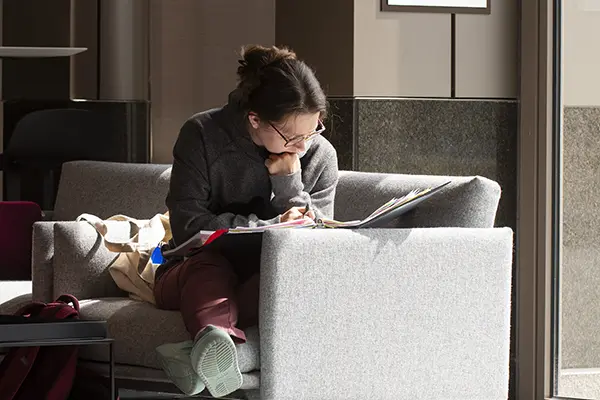 Student sitting on couch studies in student commons. 