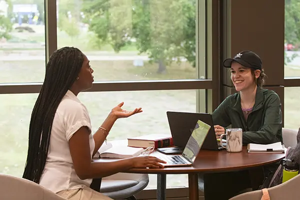 Two students talk while studying in the library.