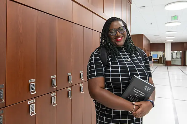 Student stands in front of lockers holding books. 