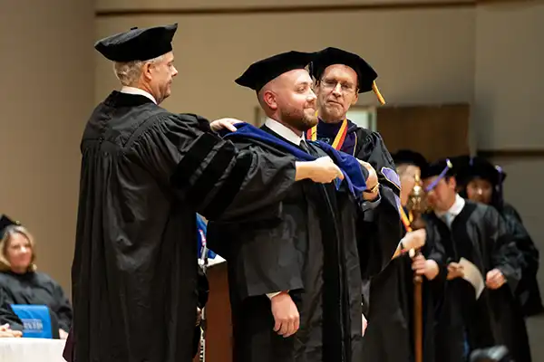 A graduate receives their caape on stage.